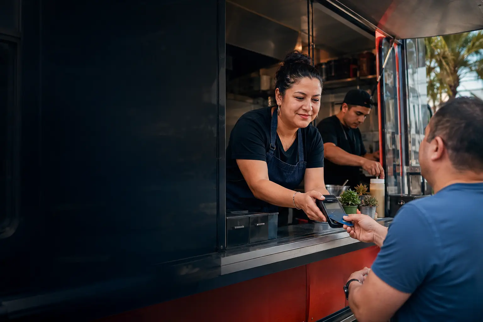 Latina food-truck owner helping a customer complete a contactless payment during lunch service